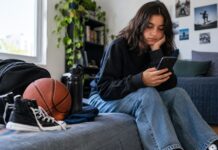 Excesso de telas reduz atividade física entre adolescentes Adolescente sentado usando celular enquanto tênis esportivo aparece ao lado